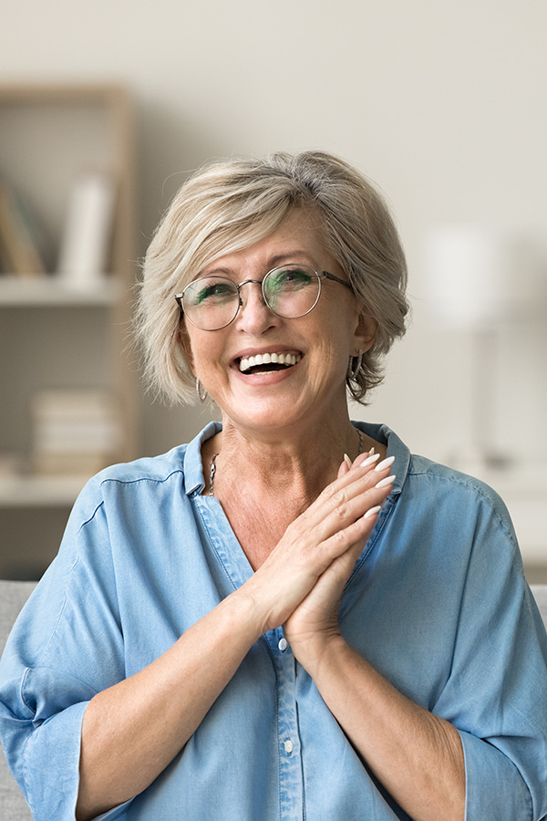 Smiling old woman with glasses with hands together