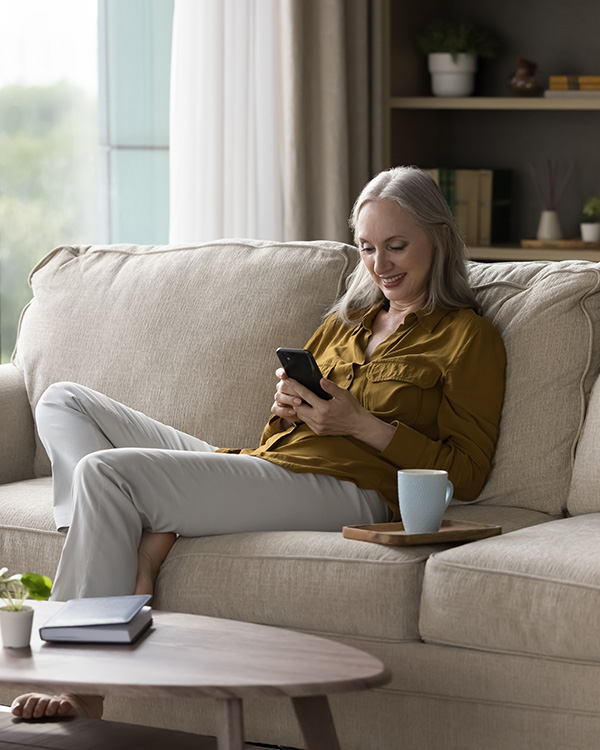 Older woman sitting at sofa smiling at her phone